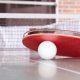 white pingpong ball beneath red table tennis paddle